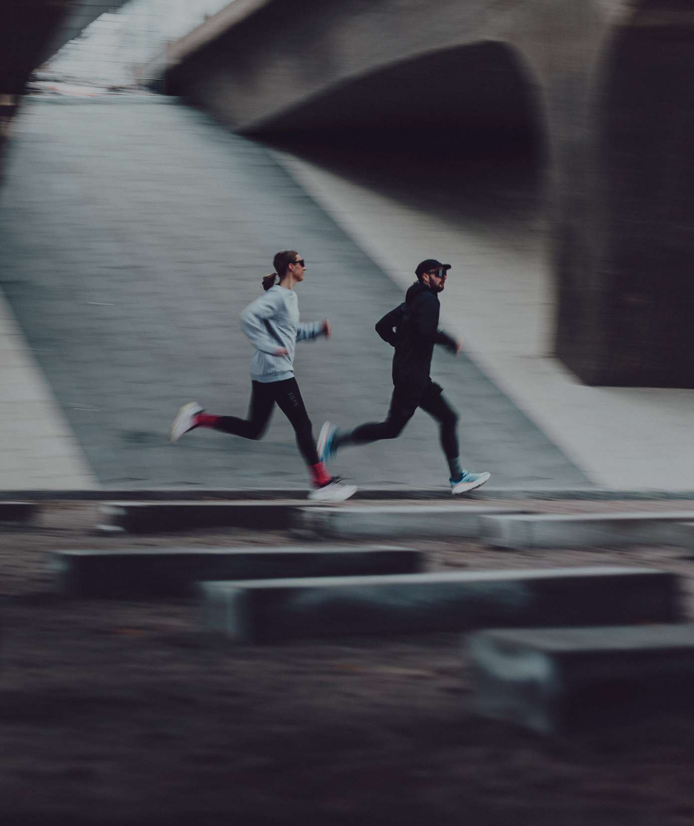 Two people running side by side on an urban pathway, wearing athletic gear.