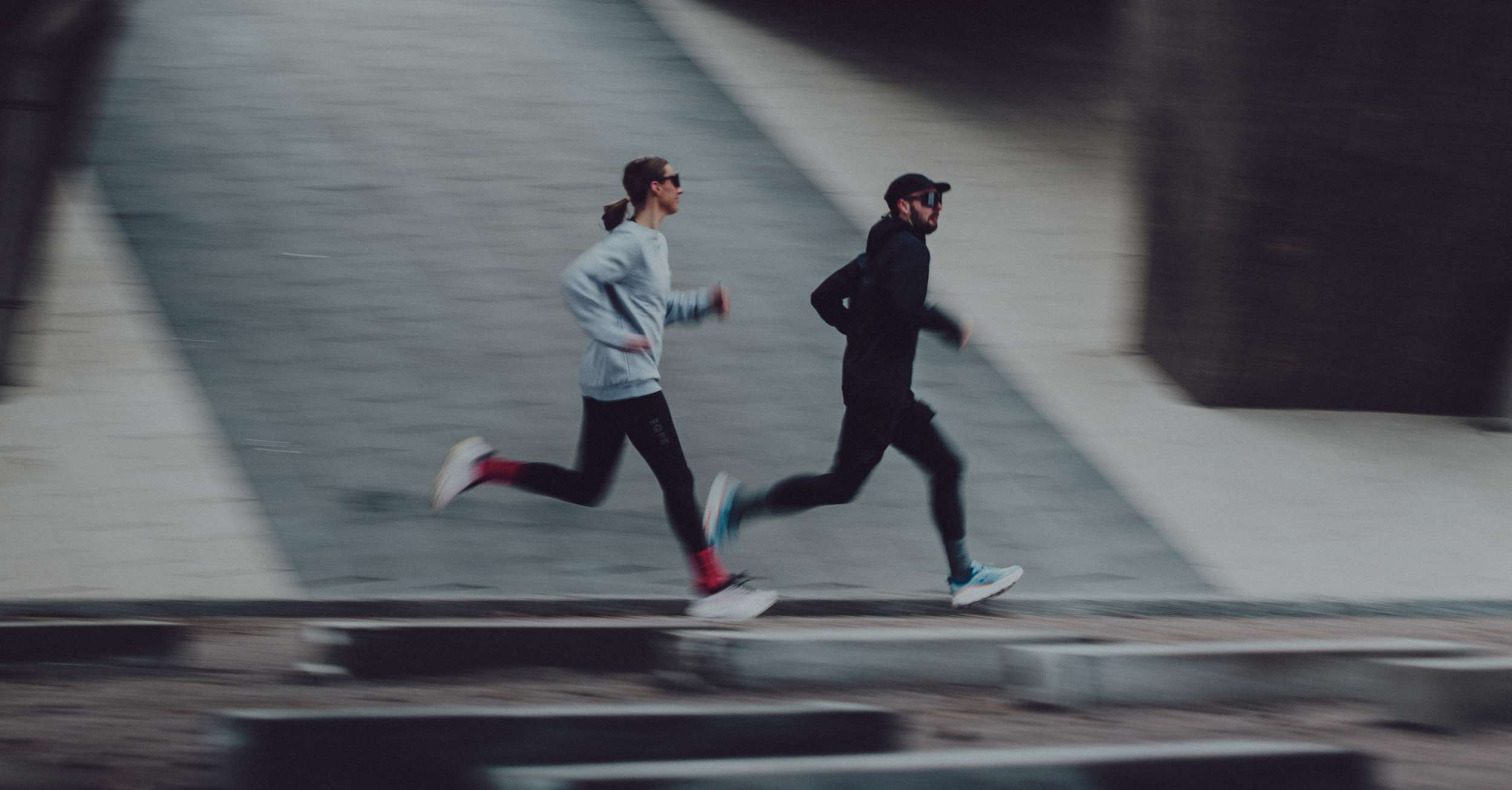 Two people running side by side on an urban pathway, wearing athletic gear.